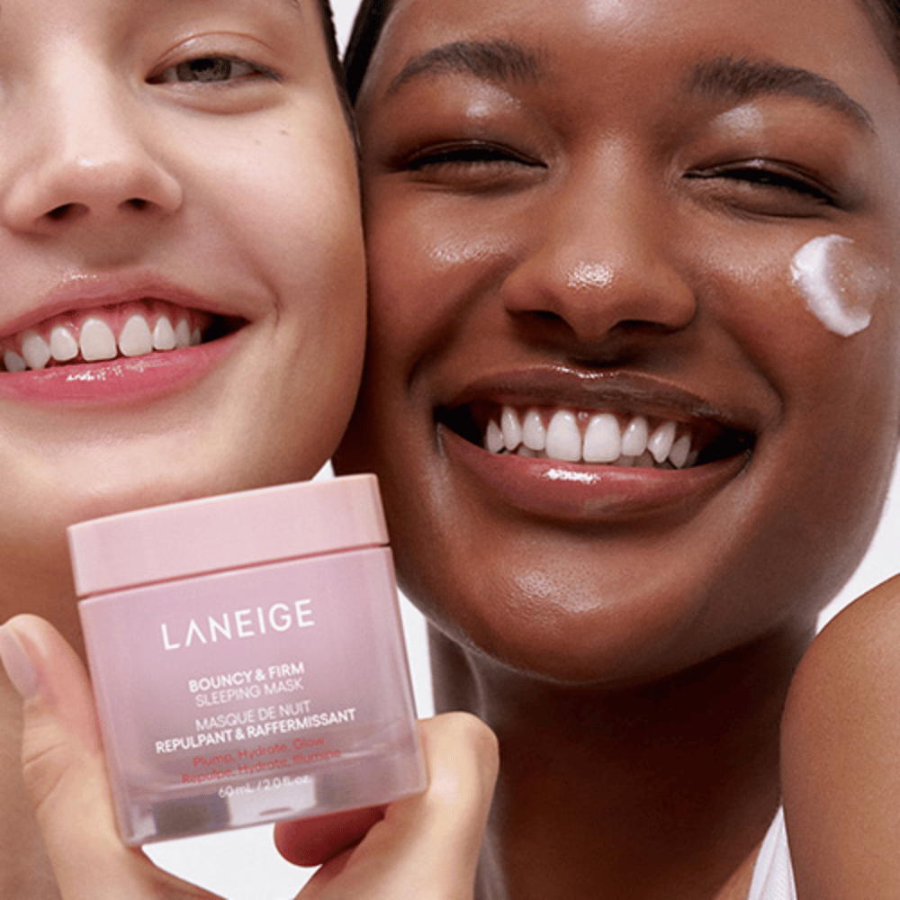 Två personer ler och håller i Laneige Bouncy & Firm Sleeping Mask. Den ena har applicerat masken på sin kind, och produkten syns tydligt i deras händer. Masken är i en rosa burk och marknadsförs som "Plump, Hydrate, Glow.