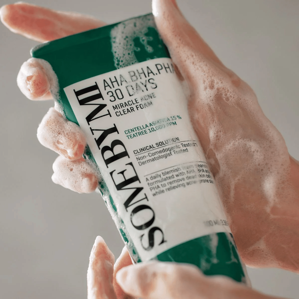 Ένα άτομο κρατάει ένα σωληνάριο "SOME BY MI AHA, BHA, PHA 30 Days Miracle Acne Clear Foam" με αφρώδες περιεχόμενο πάνω από τα χέρια του. Το προϊόν προορίζεται για καθημερινή χρήση για την καταπολέμηση της ακμής και τον καθαρισμό των πόρων με τα ενεργά συστατικά του, όπως centella, tea tree λάδι και οξέα όπως AHA, BHA και PHA.