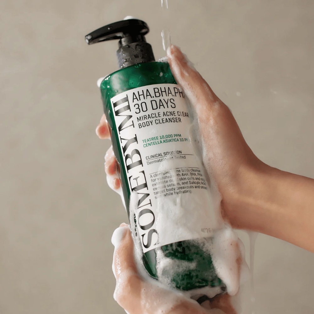 Ένα άτομο κρατάει ένα μπουκάλι SOME BY MI AHA.BHA.PHA 30 Days Miracle Acne Clear Body Cleanser. Το μπουκάλι είναι πράσινο με μια άσπρη ετικέτα και είναι καλυμμένο με αφρό από το καθαριστικό. Το άτομο πλένεται με το προϊόν ενώ το νερό τρέχει πάνω από τα χέρια.