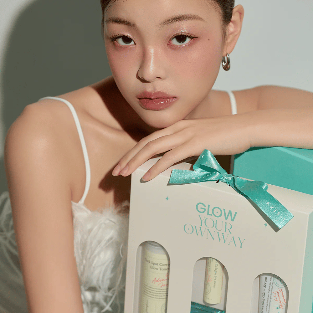 Μοντέλο με κομψό μακιγιάζ κρατά το “Glow Your Own Way” κουτί δώρου της AXIS-Y – ένα κομψό σετ περιποίησης δέρματος, τέλειο ως δώρο για εσάς ή κάποιον που αγαπάτε.