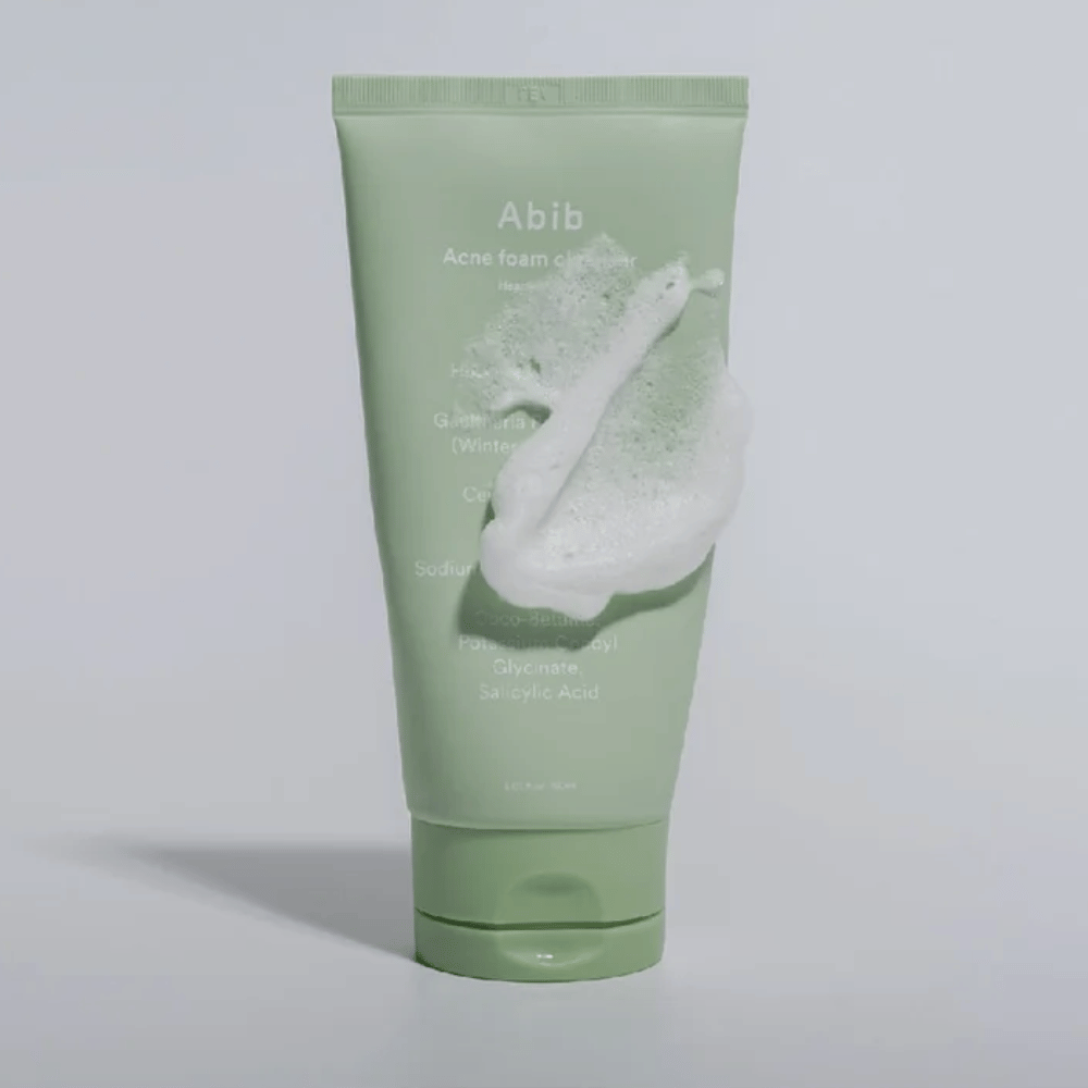 Πράσινος σωλήνας με Abib Acne Foam Cleanser Heartleaf, καλυμμένος με λευκό αφρό που εικονογραφεί την αφρώδη καθαριστική επίδραση. Το προϊόν περιέχει εκχύλισμα καρδιοφύλλου και σαλικυλικό οξύ για δέρμα επιρρεπές στην ακμή.