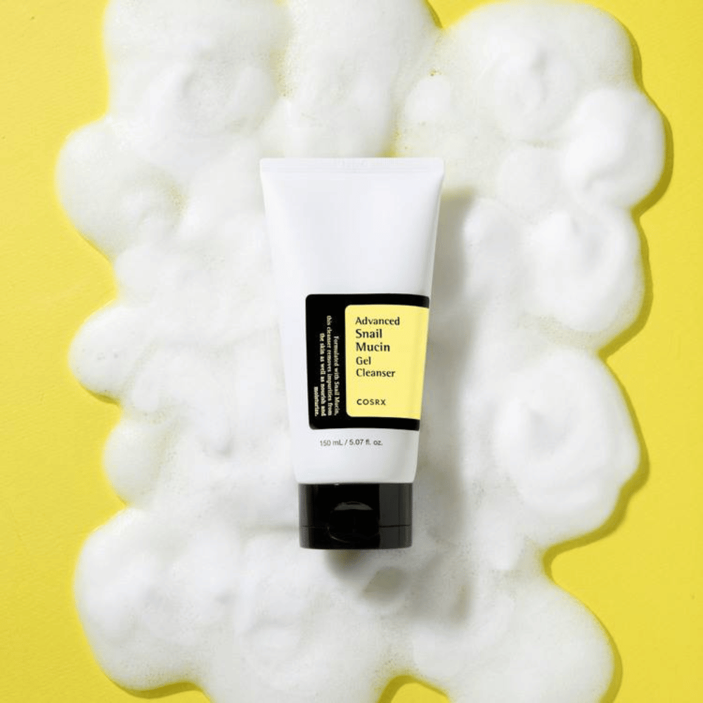 COSRX Advanced Snail Mucin Gel Cleanser 150 ml περιτριγυρισμένο από άφθονο αφρό σε κίτρινο φόντο – απαλός κορεάτικος καθαρισμός προσώπου με βλέννα σαλιγκαριού για ενυδάτωση και λάμψη.