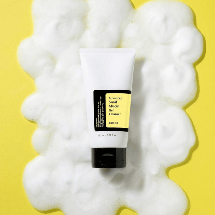 COSRX Advanced Snail Mucin Gel Cleanser 150 ml περιτριγυρισμένο από άφθονο αφρό σε κίτρινο φόντο – απαλός κορεάτικος καθαρισμός προσώπου με βλέννα σαλιγκαριού για ενυδάτωση και λάμψη.