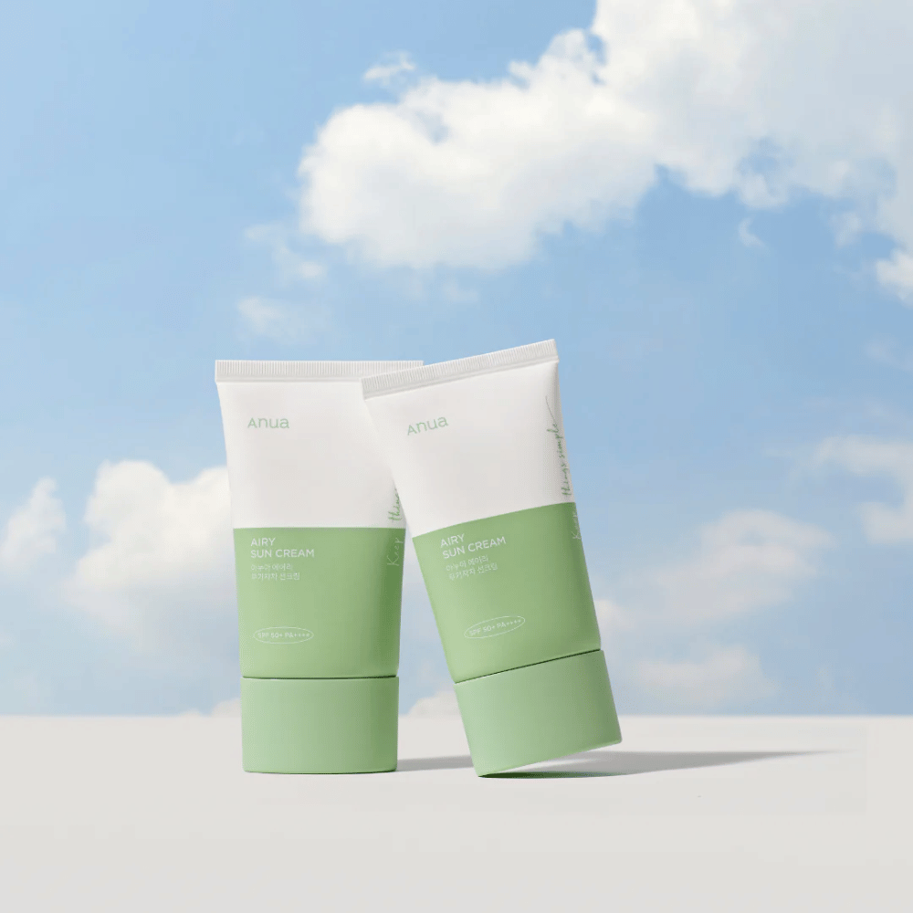 Δύο σωλήνες του Anua Airy Sun Cream απέναντι από έναν ουρανό με λευκά σύννεφα.