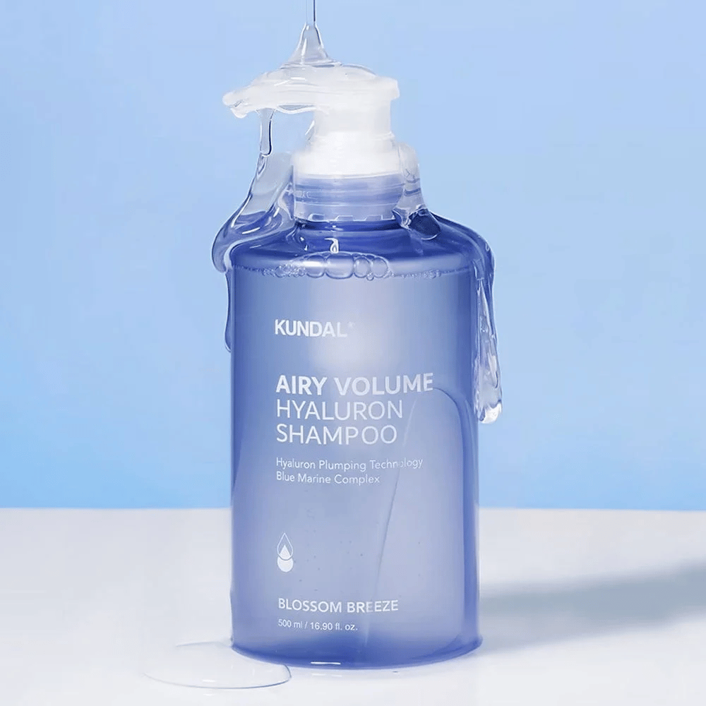 KUNDAL Airy Volume Hyaluron Shampoo Blossom Breeze σε μπλε μπουκάλι αντλίας, με υαλουρονικό και Blue Marine Complex, φωτογραφημένο με τρεχούμενο νερό.
