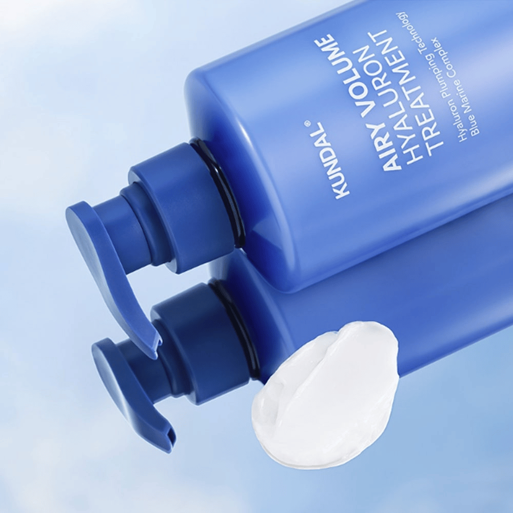 KUNDAL Airy Volume Hyaluron Treatment σε μπλε μπουκάλι με αντλία που κείται, με λευκό κρεμώδες προϊόν ορατό δίπλα.