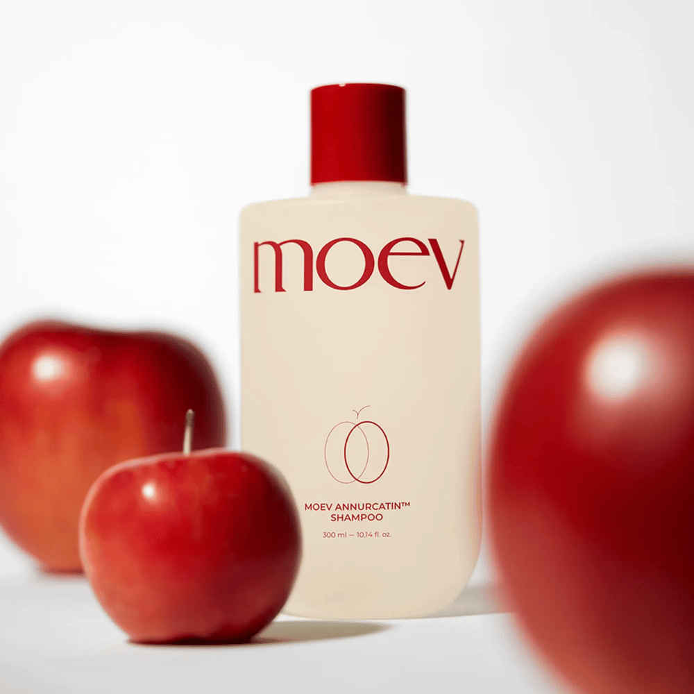 MOEV Annurcatin Shampoo τοποθετημένο ανάμεσα σε κόκκινα μήλα – εμπνευσμένο από τα αντιοξειδωτικά του μήλου Annurca που προσφέρουν πιο δυνατά, υγιή και λαμπερά μαλλιά.