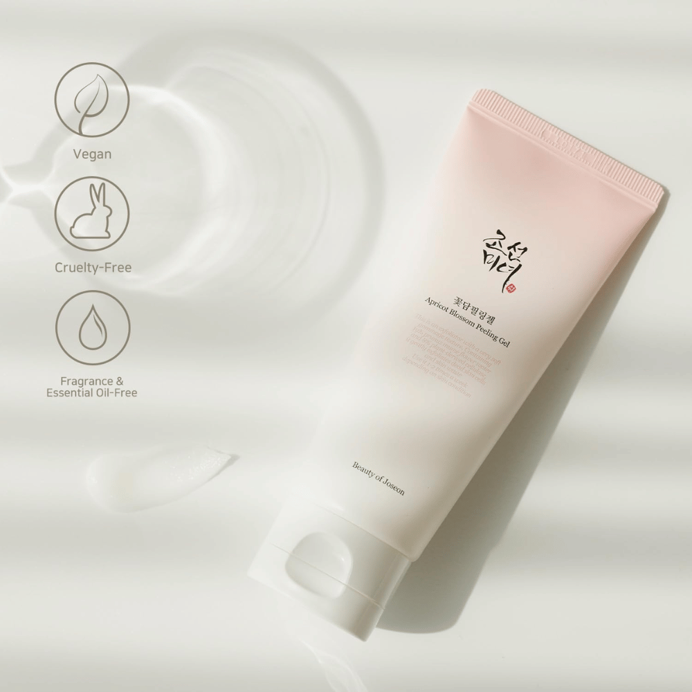 Ένας σωλήνας με Apricot Blossom Peeling Gel βρίσκεται σε ανακλαστική επιφάνεια με εικονίδια που υποδεικνύουν ότι το προϊόν είναι βίγκαν, φιλικό προς τα ζώα και απαλλαγμένο από άρωμα και αιθέρια έλαια.