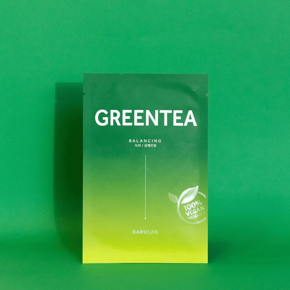 Μια συσκευασία από την BARULAB για μια μάσκα "GREENTEA Balancing", με την ένδειξη "100% Vegan Product". Το χρώμα της συσκευασίας μεταβαίνει από σκούρο πράσινο στην κορυφή σε πιο ανοιχτό πράσινο στο κάτω μέρος, σε ένα ομοιόμορφο πράσινο φόντο.