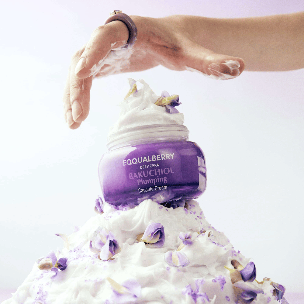 EQQUALBERRY Bakuchiol Plumping Capsule Cream τοποθετημένο πάνω σε μια στοίβα από χτυπημένη κρέμα με πέταλα λουλουδιών – συμβολίζει την ενυδάτωση και τη φροντίδα.
