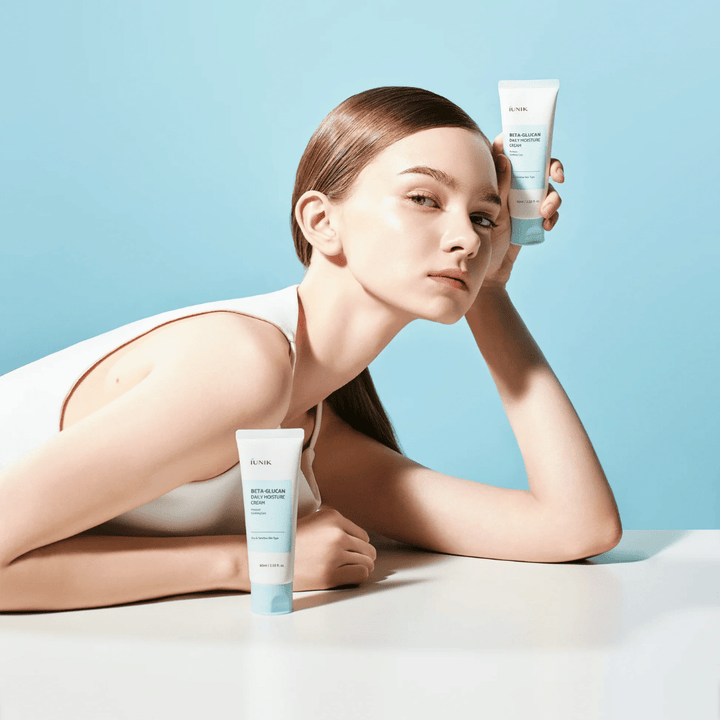 Lifestyle εικόνα όπου ένα μοντέλο ποζάρει με το iUNIK Beta-Glucan Daily Moisture Cream μπροστά σε ανοιχτό γαλάζιο φόντο. Η εικόνα αποπνέει μια καθαρή, φρέσκια και ενυδατική αίσθηση, ενώ παράλληλα το προϊόν προβάλλεται καθαρά.