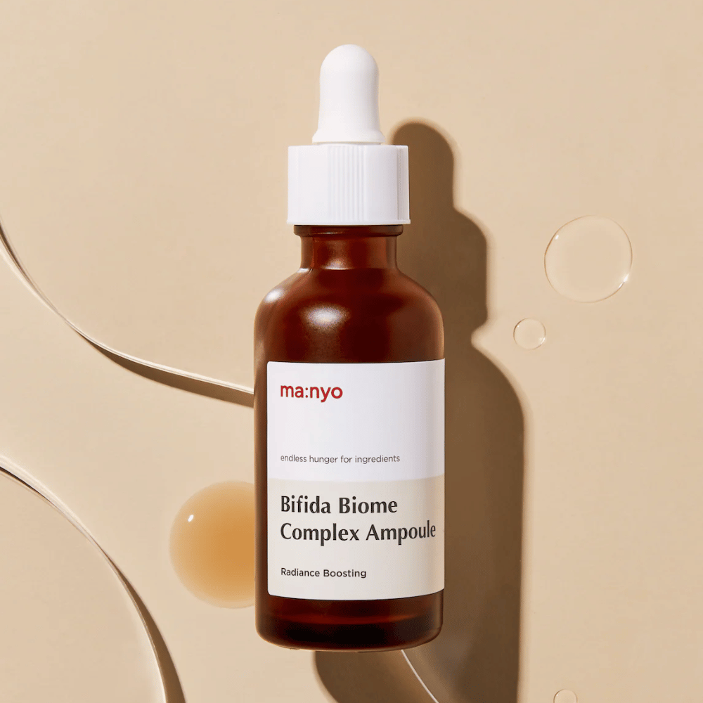 Κομψή εικόνα προϊόντος του ma:nyo Bifida Biome Complex Ampoule με έμφαση στον σχεδιασμό του μπουκαλιού και στις σταγόνες serum στο φόντο.