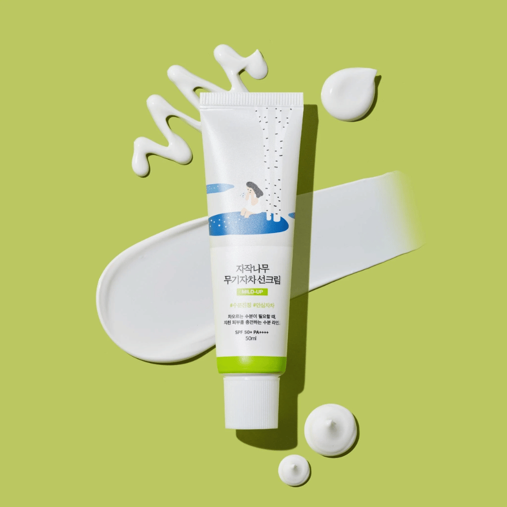 Birch Juice Moisturizing Mild Up Sunscreen – λευκό σωληνάριο με πράσινη βάση σε πράσινο φόντο, περιτριγυρισμένο από απλωμένη αντηλιακή κρέμα και σταγόνες, SPF 50+ PA++++, 50 ml.