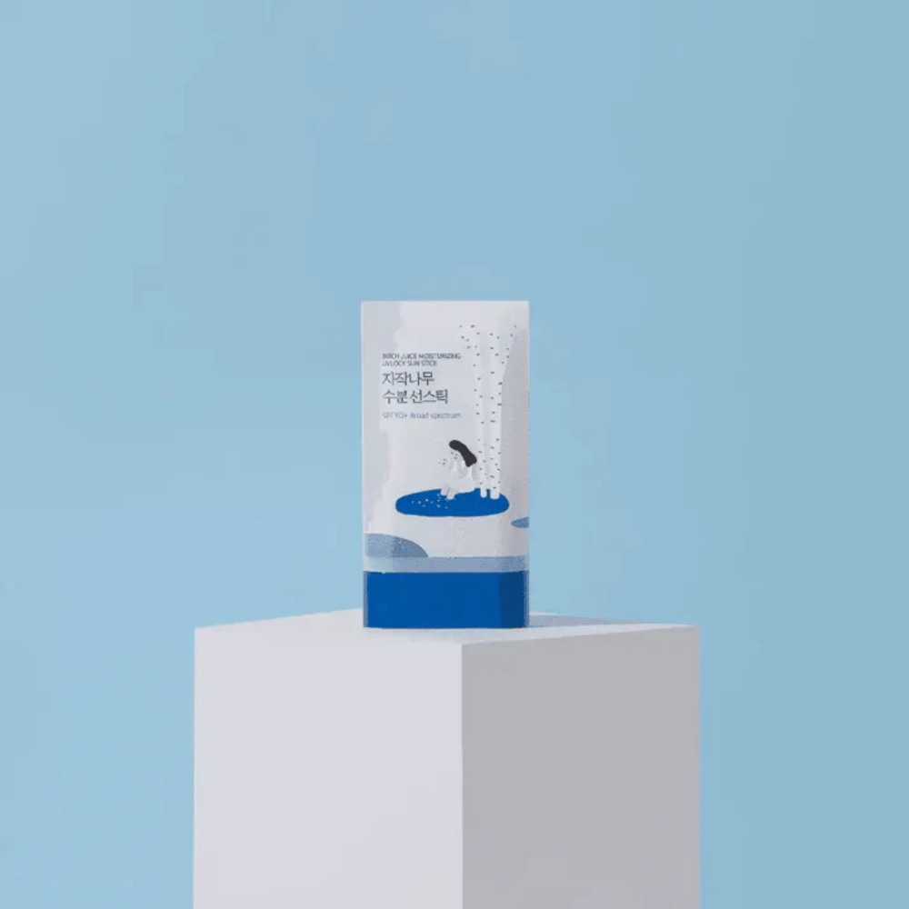Το ROUND LAB Birch Juice Moisturizing Sun Stick SPF50+ στέκεται σε βάθρο με μπλε φόντο – ενυδατική αντηλιακή προστασία σε μορφή στικ