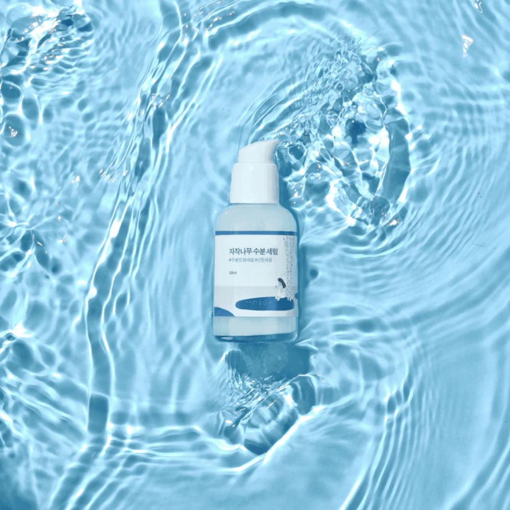 Round Lab Birch Juice Moisturizing Serum σε μπουκάλι αντλίας που επιπλέει σε μπλε νερό με αντανακλάσεις ηλιακού φωτός.