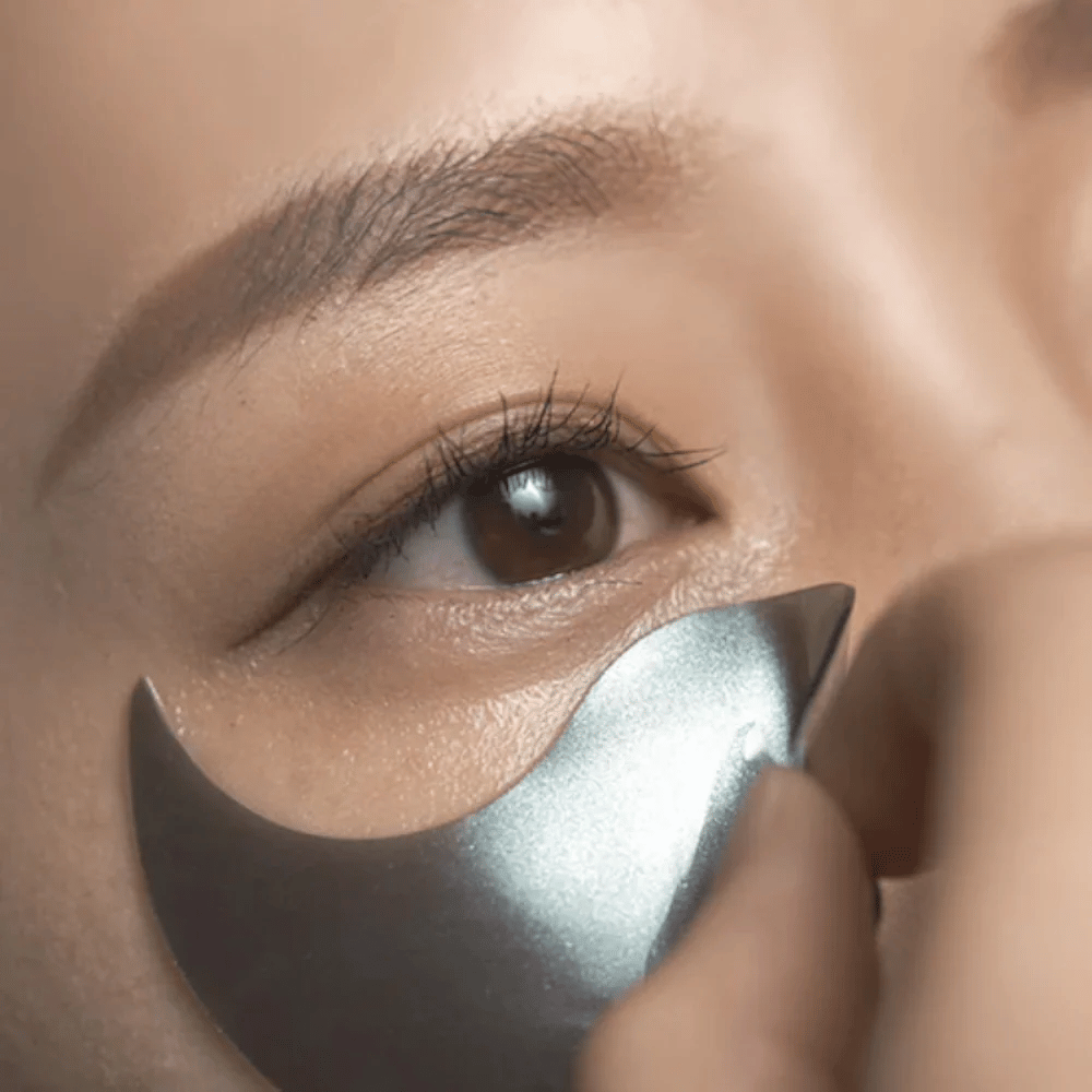 Λεπτομερής εικόνα όπου ένα μαύρο hydrogel eye patch εφαρμόζεται κάτω από το μάτι. Η εικόνα δείχνει την τέλεια εφαρμογή και τη δροσερή αίσθηση γύρω από την περιοχή των ματιών.