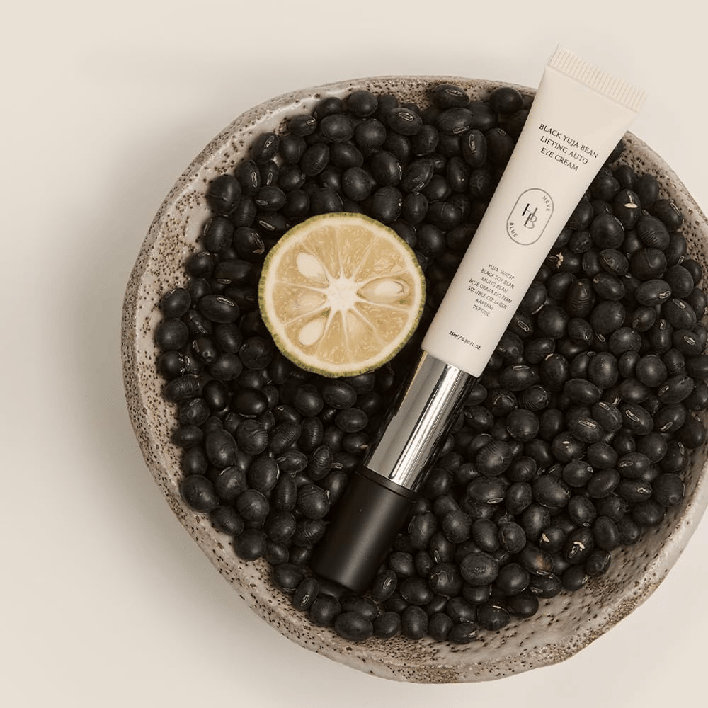 Black Yuja Bean Lifting Auto Eye Cream που βρίσκεται σε ένα μπολ γεμάτο με μαύρα φασόλια και ένα μισό εσπεριδοειδές - μια οπτική αναπαράσταση των φυσικών συστατικών του προϊόντος.