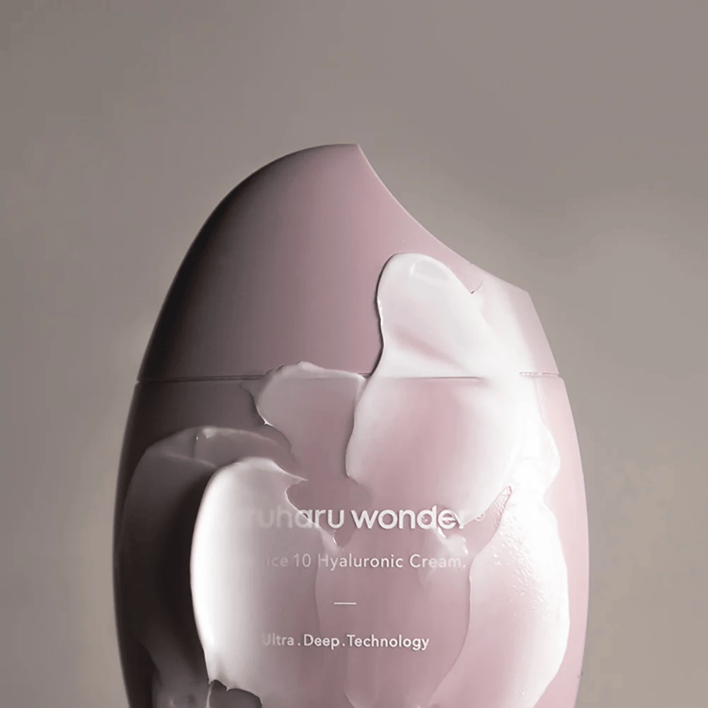 Η εικόνα δείχνει ένα βάζο με "Haruharu Wonder Black Rice 10 Hyaluronic Cream", το οποίο καλύπτεται εν μέρει από μια παχιά, διαφανή κρέμα. Το κείμενο στην εικόνα υποδηλώνει τη χρήση προηγμένης τεχνολογίας για βαθιά ενυδάτωση του δέρματος. Ο σχεδιασμός είναι μοντέρνος και μινιμαλιστικός.