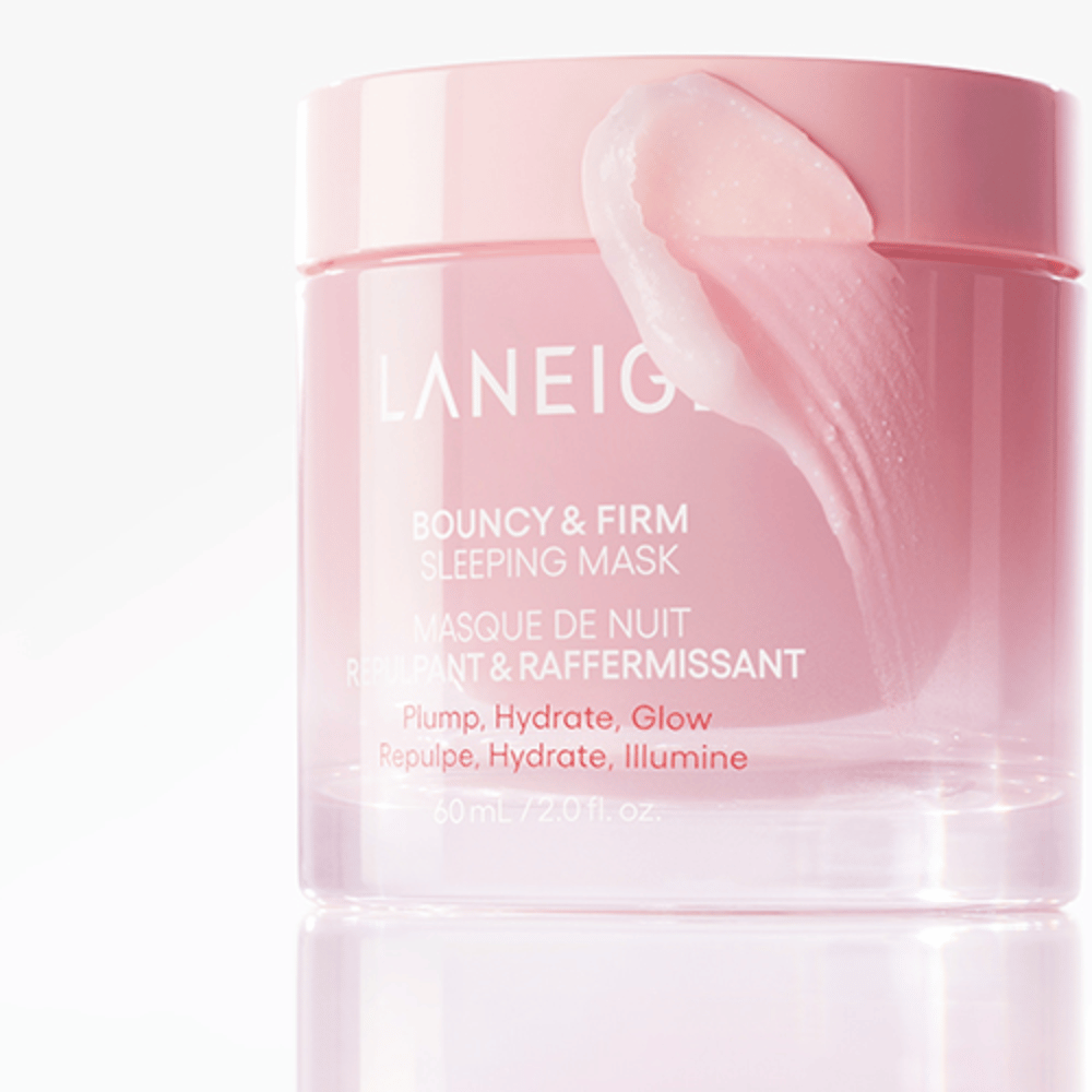 Κοντινό πλάνο του Laneige Bouncy & Firm Sleeping Mask σε ένα ροζ βάζο, με μέρος της μάσκας να εφαρμόζεται στην άκρη του καπακιού. Το προϊόν προορίζεται για να προσφέρει όγκο, ενυδάτωση και λάμψη. Το βάζο περιέχει 60 ml και έχει το κείμενο "Plump, Hydrate, Glow."