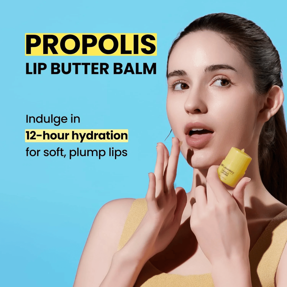 Μια γυναίκα εφαρμόζει το CNP Laboratory Propolis Lip Butter Balm, προβαλλόμενο σε μπλε φόντο. Το προϊόν υπόσχεται 12 ώρες ενυδάτωσης για απαλά και γεμάτα χείλη, όπως φαίνεται με έναν κίτρινο σωλήνα που κρατά στο χέρι της.