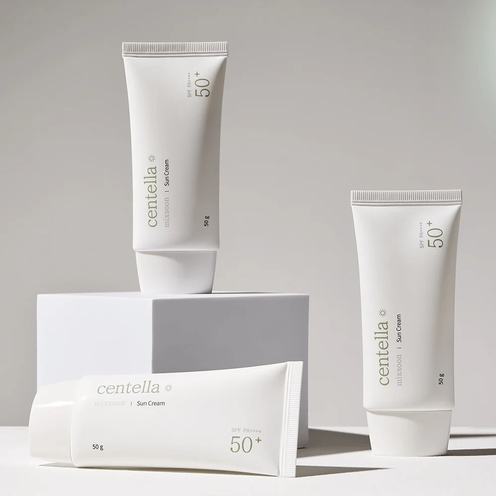 Τρεις συσκευασίες Centella Sun Cream SPF 50+ PA++++ τοποθετημένες αισθητικά σε λευκά βάθρα. Δύο σωληνάρια στέκονται όρθια και ένα είναι ξαπλωμένο, όλα με λευκό, μινιμαλιστικό σχεδιασμό και πράσινες λεπτομέρειες κειμένου.