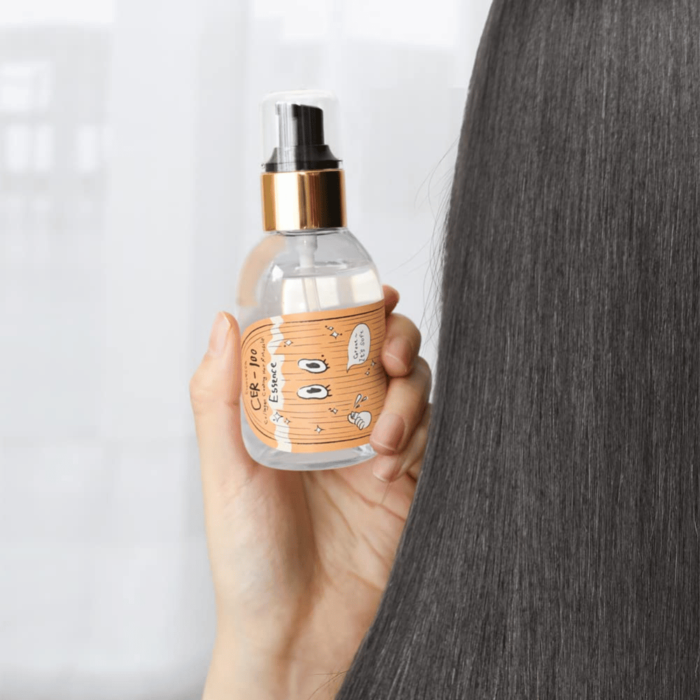 Άτομο κρατά το CER-100 Hair Essence δίπλα σε μακριά, λαμπερά μαλλιά για να δείξει απαλότητα και φροντίδα.