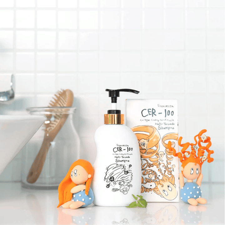 Το Elizavecca CER-100 Shampoo και το κουτί του παρουσιάζονται σε περιβάλλον μπάνιου δίπλα σε βούρτσα μαλλιών και διακοσμητικές φιγούρες. Η εικόνα αποδίδει μια καθημερινή ρουτίνα περιποίησης μαλλιών και τη χρήση του προϊόντος στο οικιακό περιβάλλον.