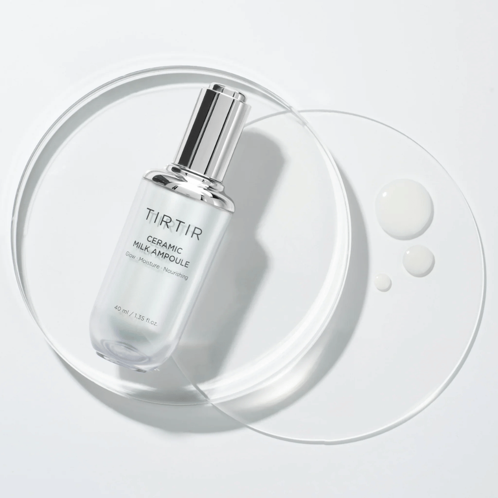 Ένα διαφανές μπουκάλι TIRTIR Ceramic Milk Ampoule σε μια γυάλινη πλάκα με σταγόνες, σε λευκό φόντο, αναδεικνύει τη λάμψη, την υγρασία και τη θρέψη.