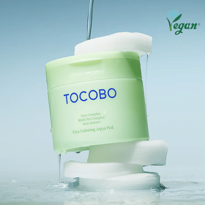 Το TOCOBO Cica Calming Aqua Pad τοποθετημένο ανάμεσα σε toner pads με essence που ρέει. Το σύμβολο vegan τονίζει τη vegan σύνθεση του προϊόντος και το φιλικό προς το δέρμα προφίλ του.