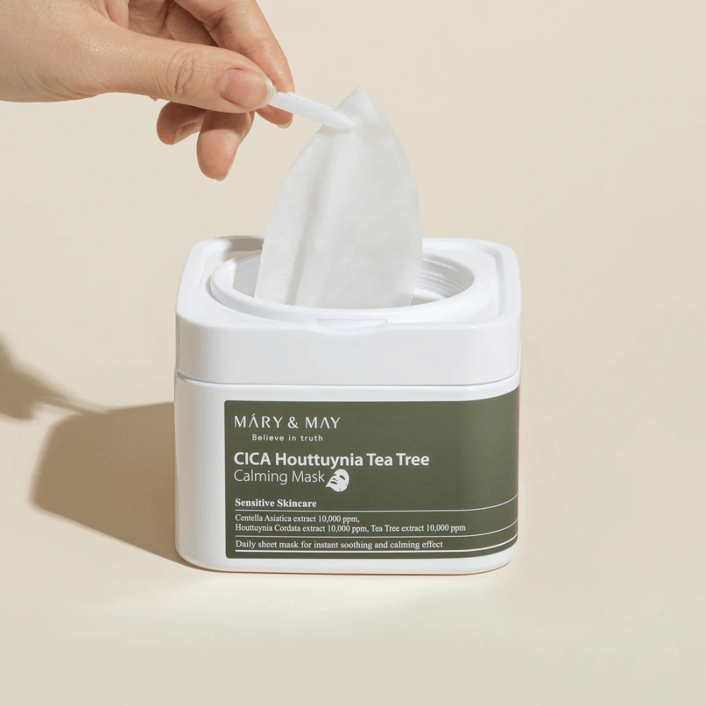 Χέρι που τραβάει μια sheet μάσκα από το βάζο Mary & May Cica Houttuynia Tea Tree Calming Mask – καταπραϋντική μάσκα προσώπου για ευαίσθητο δέρμα με Cica και εκχύλισμα Tea Tree.