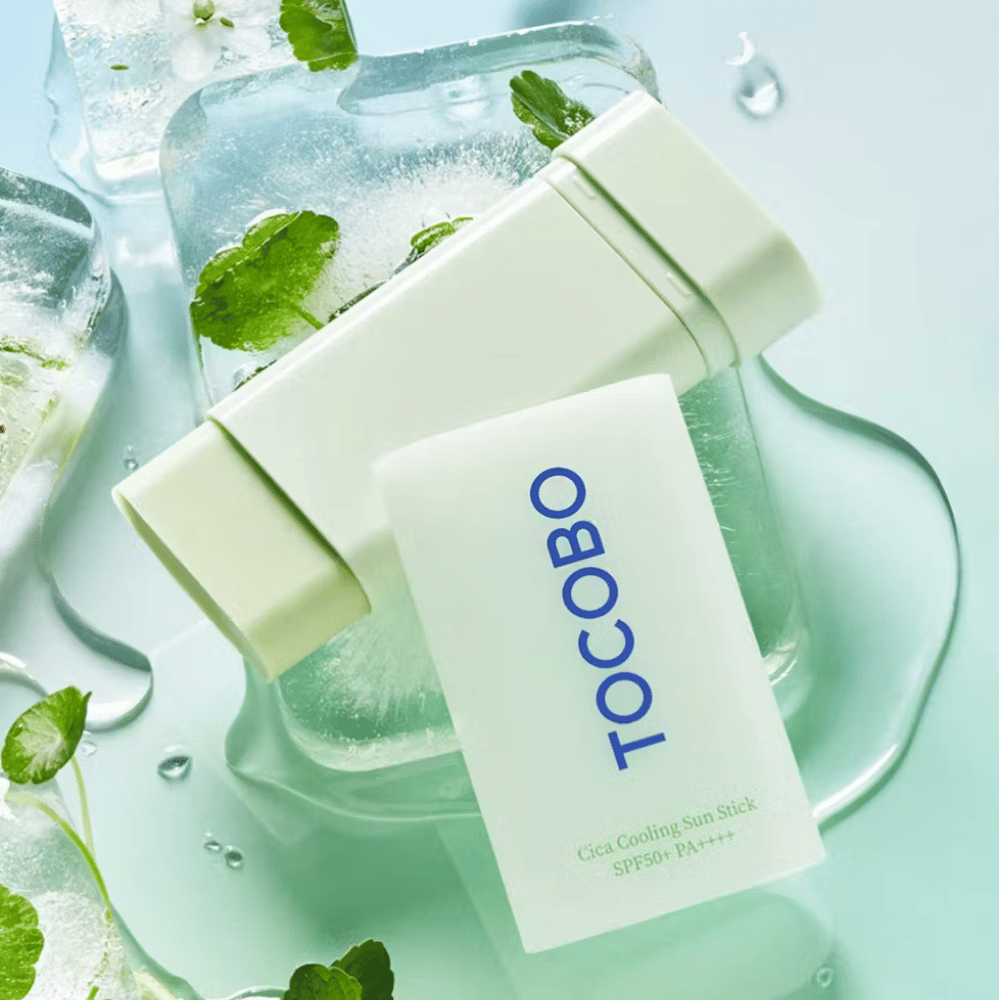 Tocobo Cica Cooling Sun Stick SPF50+ PA++++ σε παγάκια με πράσινα φύλλα φυτών, που μεταφέρει μια αίσθηση δροσιάς και αναζωογόνησης.