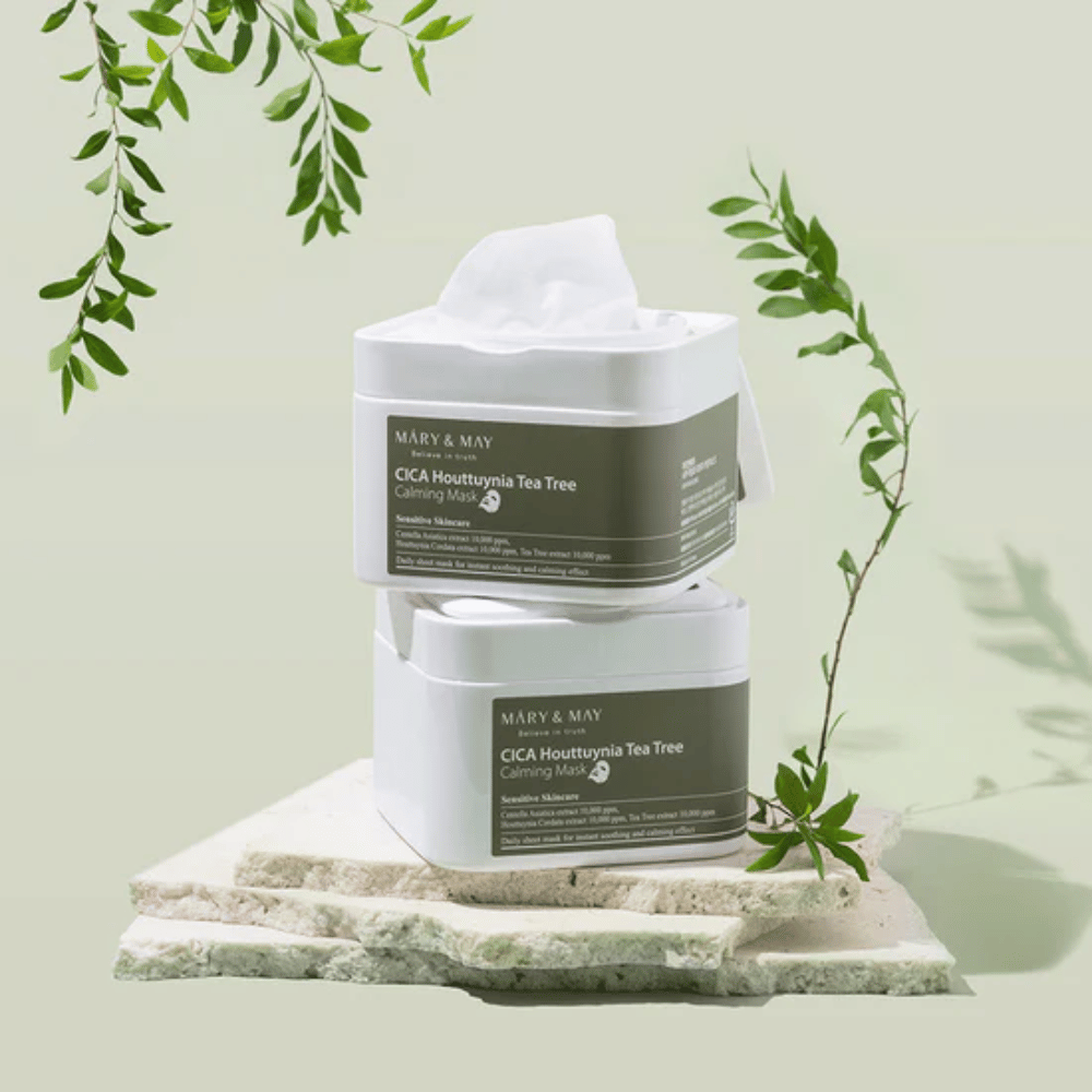 Δύο βάζα Mary & May Cica Houttuynia Tea Tree Calming Mask τοποθετημένα σε φυσική πέτρα με πράσινες λεπτομέρειες φυτών – καταπραϋντικές sheet μάσκες για ευαίσθητο δέρμα.