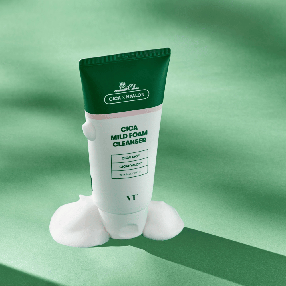 Σωλήνας με VT Cica Mild Foam Cleanser τοποθετημένος σε πράσινο υπόστρωμα με αφρό γύρω από τη βάση. Το προϊόν έχει πράσινο και λευκό σχέδιο και προωθείται με CICALIAO™ και CICAHYALON™.