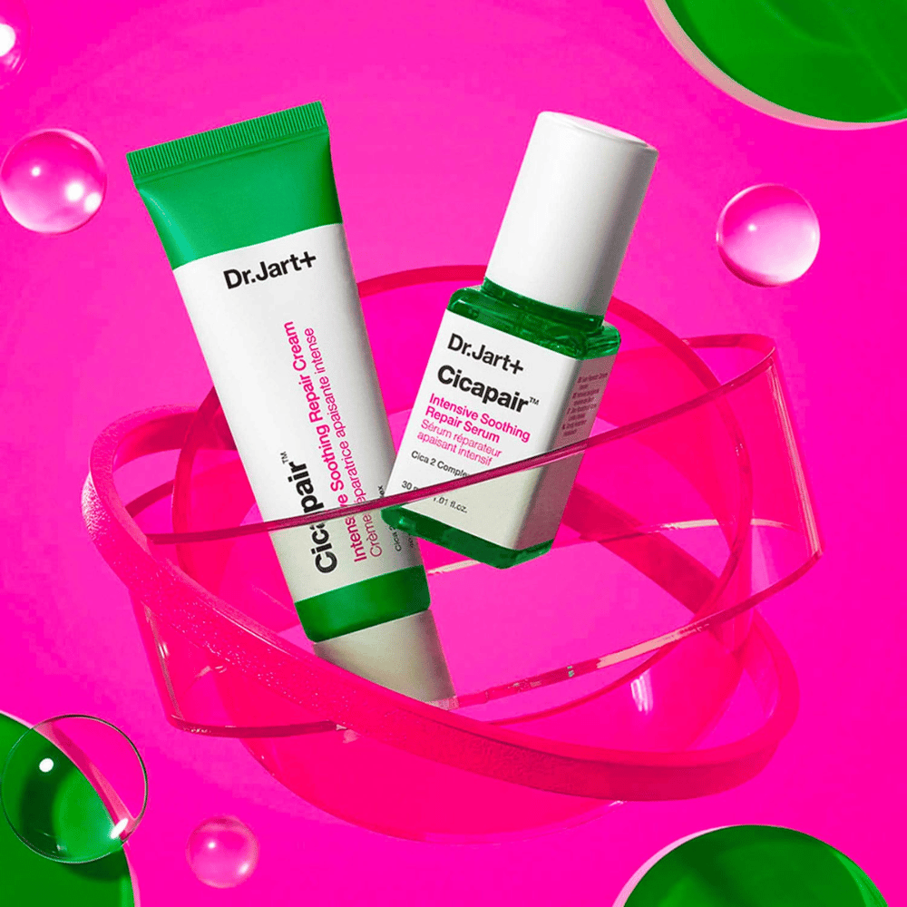 Dr.Jart+ Cicapair Intensive Soothing Repair Cream και Serum σε πράσινες συσκευασίες, που βρίσκονται πάνω σε μια ροζ κυκλική βάση. Τα προϊόντα έχουν σχεδιαστεί για να καταπραΰνουν και να επισκευάζουν ερεθισμένο δέρμα.