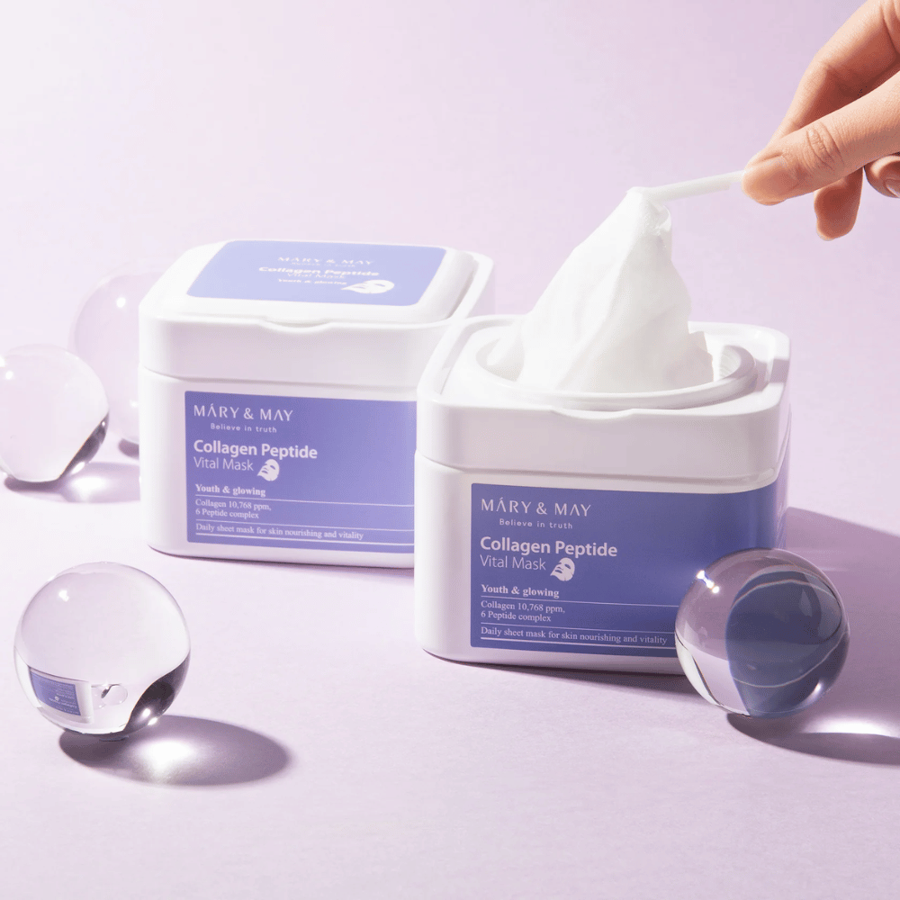Ένα χέρι παίρνει μια μάσκα από ένα βάζο με MARY & MAY Collagen Peptide Vital Mask. Η μάσκα προορίζεται για καθημερινή χρήση για να παρέχει θρέψη και λάμψη στο δέρμα, με κολλαγόνο και πεπτίδια για να υποστηρίξουν τη νεανικότητα του δέρματος.