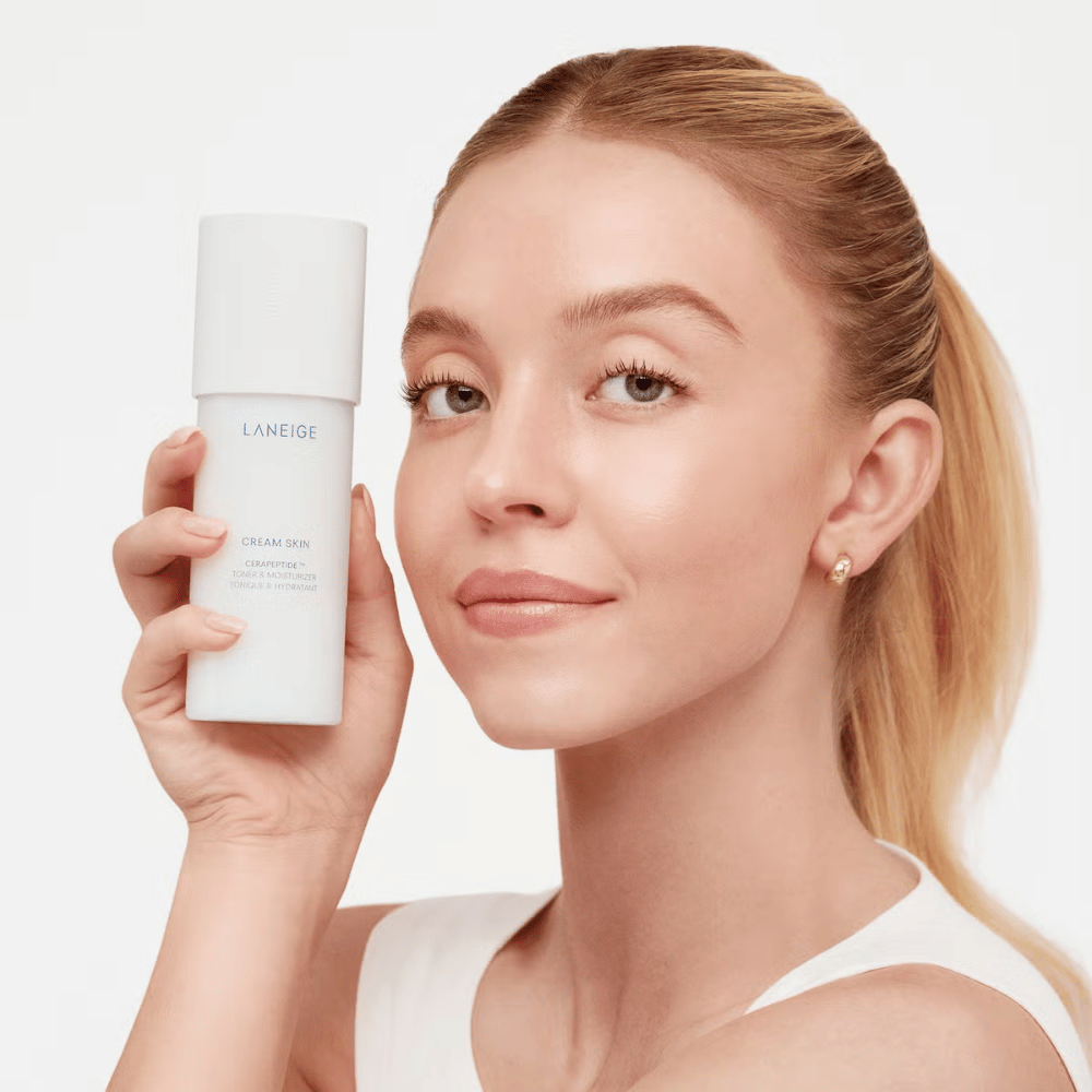 Ένα άτομο κρατάει Laneige Cream Skin Cerapeptide Refiner σε ένα λευκό μπουκάλι. Το άτομο χαμογελά και παρουσιάζει το προϊόν, το οποίο προωθείται ως ενυδατικό τόνερ και προϊόν περιποίησης δέρματος.