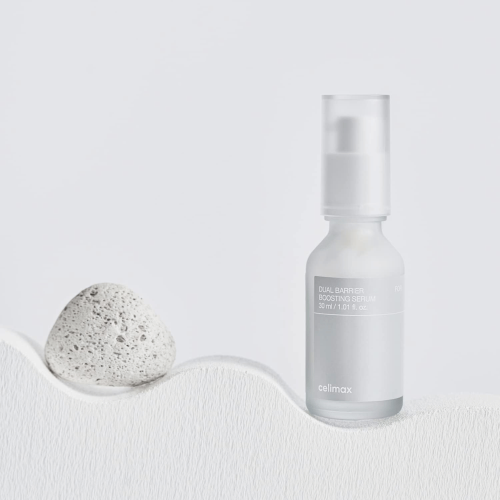 Celimax Dual Barrier Boosting Serum τοποθετημένο σε ύφασμα με πέτρα, ήρεμη εικόνα προϊόντος που σηματοδοτεί ενυδάτωση και ενισχυμένο φραγμό του δέρματος.