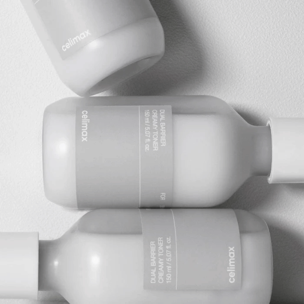 Τρία ξαπλωμένα μπουκάλια από Celimax Dual Barrier Creamy Toner σε μινιμαλιστικό σχέδιο με γκρι ετικέτα και απαλό φως – ιδανικό για ευαίσθητο και ξηρό δέρμα.