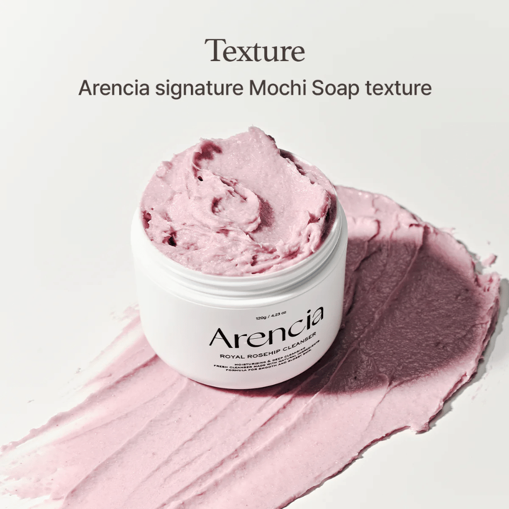 Βάζο με Arencia Royal Rosehip Cleanser φαίνεται πάνω σε απλωμένο ροζ καθαριστικό με υφή σαν μοτσί. Το κείμενο από πάνω περιγράφει το προϊόν ως την υπογραφή υφής της Arencias.