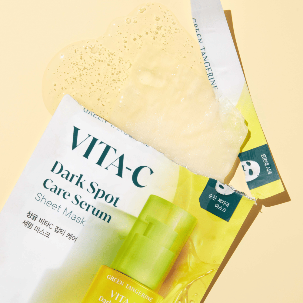 Ανοιγμένη συσκευασία του VITA-C Dark Spot Care Serum Sheet Mask με μία μάσκα προσώπου από πάνω και ένα πράσινο μπουκάλι serum, όλα σε κίτρινο φόντο.