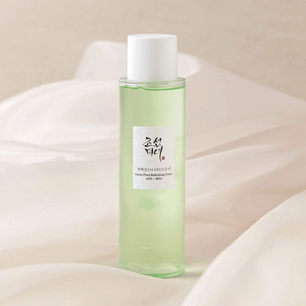 Ένα μπουκάλι με το "Green Plum Refreshing Toner" AHA + BHA στέκεται σε ένα απαλό, φωτεινό φόντο. Το προϊόν έχει ένα πράσινο υγρό που αντικατοπτρίζει τη φρεσκάδα και τη φυσικότητα. Η ετικέτα είναι λευκή με μαύρες και κόκκινες πινελιές, προσφέροντας μια κομψή και καθαρή εμφάνιση.