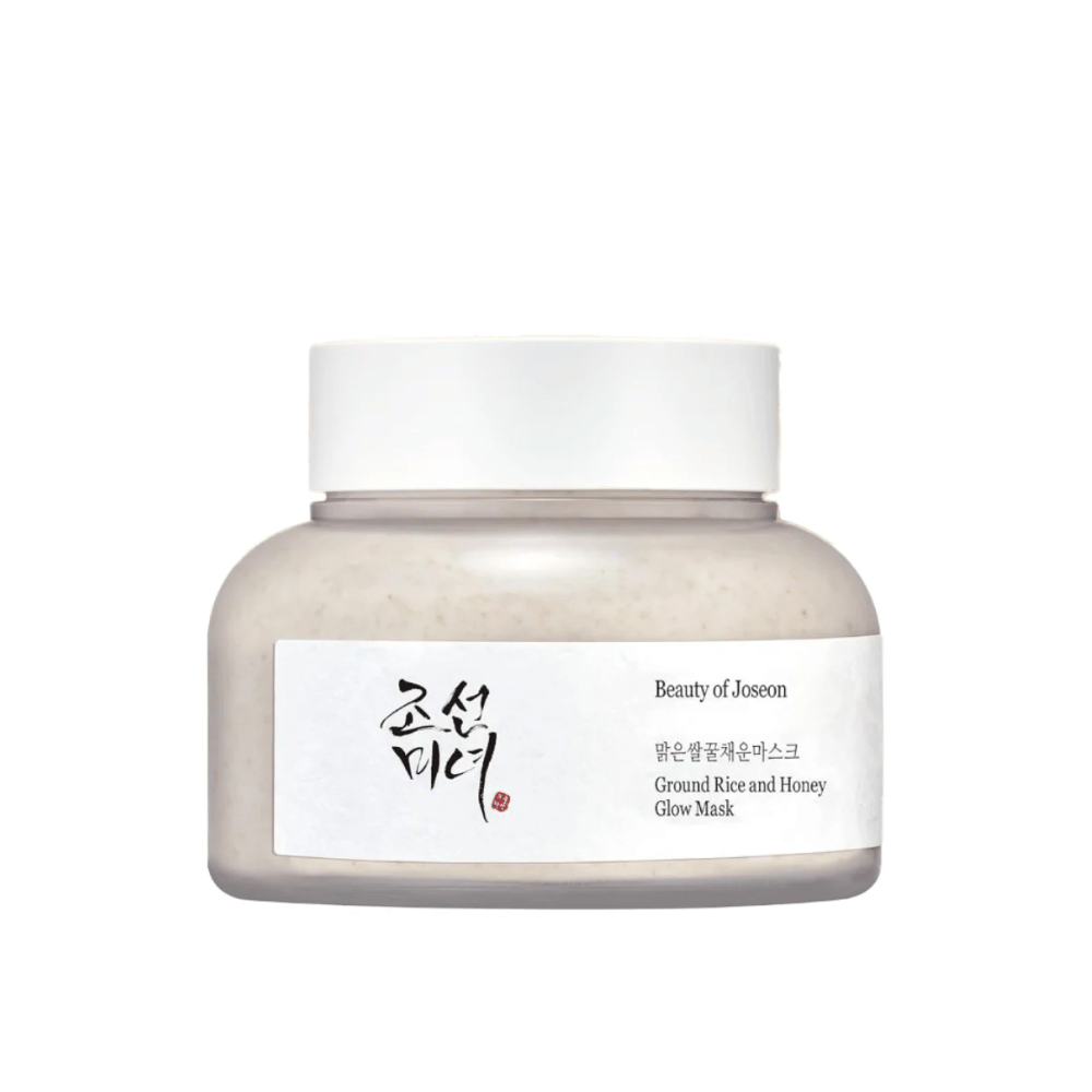 Ένα βάζο "Beauty of Joseon Ground Rice and Honey Glow Mask". Η συσκευασία είναι απλή με ένα λευκό καπάκι και μια ετικέτα που παρουσιάζει το όνομα του προϊόντος και τα συστατικά τόσο στα κορεατικά όσο και στα αγγλικά. Το προϊόν έχει σχεδιαστεί για να δίνει λάμψη και θρέψη στο δέρμα.