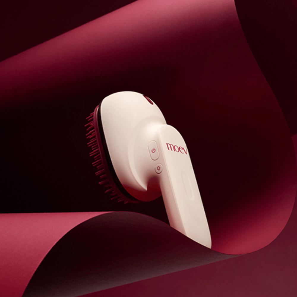 MOEV Hair Steamer Pro σε κομψό σχεδιασμό με κόκκινο φόντο. Καινοτόμα βούρτσα περιποίησης μαλλιών που χρησιμοποιεί ατμό και θερμότητα για να προσφέρει λάμψη, απαλότητα και ενισχυμένη υγεία των μαλλιών.