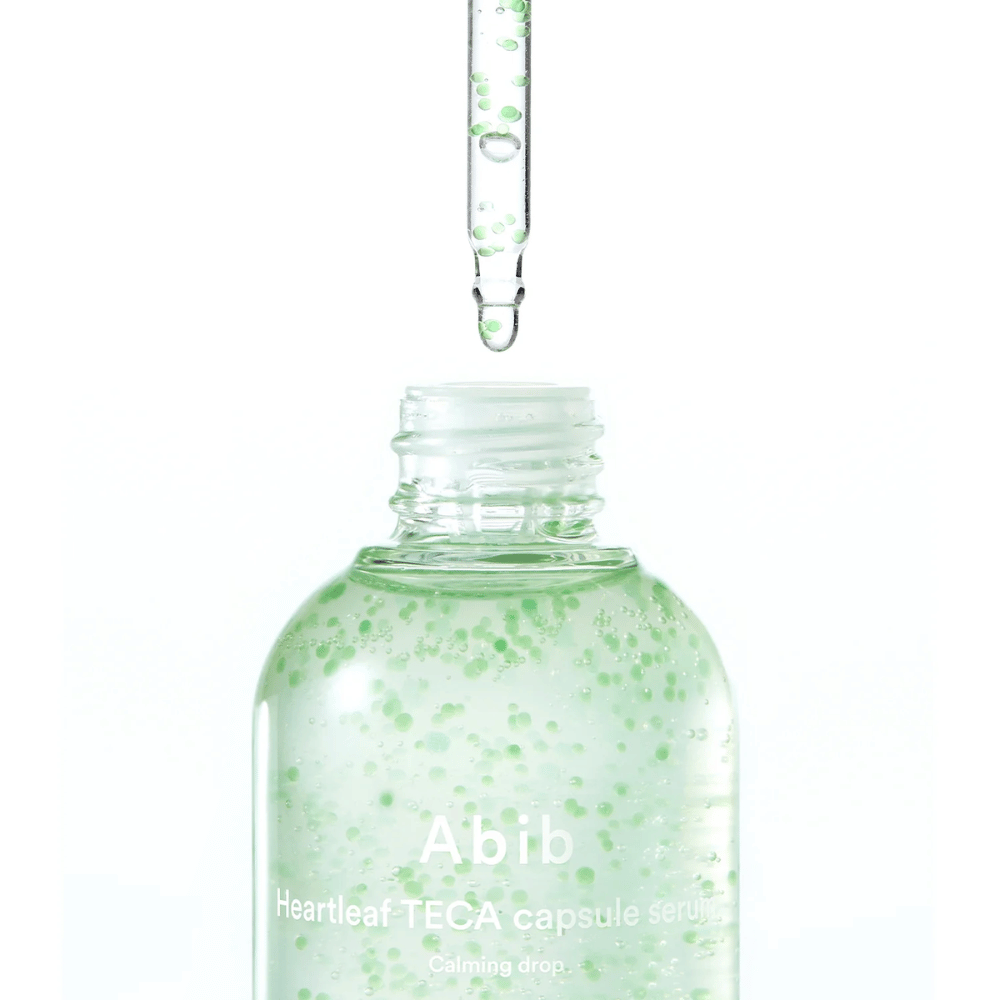 Μινιμαλιστικό κοντινό πλάνο του μπουκαλιού serum και της πιπέτας, όπου η διάφανη σύνθεση με πράσινες κάψουλες βρίσκεται στο επίκεντρο πάνω σε ανοιχτόχρωμο φόντο.