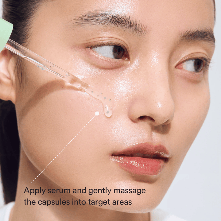 Κοντινό πλάνο μοντέλου που εφαρμόζει το serum με πιπέτα ενώ οι πράσινες κάψουλες γίνονται μασάζ στην επιδερμίδα για καταπραϋντική και ενυδατική δράση.