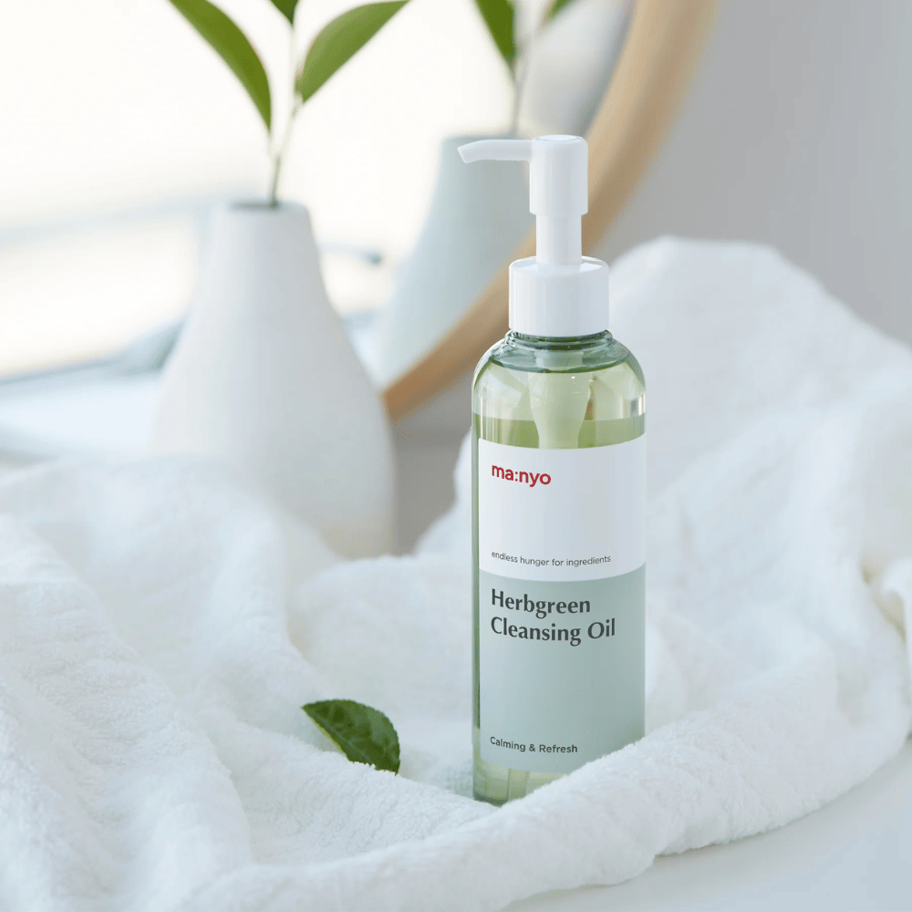 ma:nyo Herbgreen Cleansing Oil σε μπουκάλι με αντλία τοποθετημένο σε λευκή πετσέτα, καταπραϋντικό καθαριστικό λάδι με συστατικά από βότανα για ήπιο καθαρισμό προσώπου