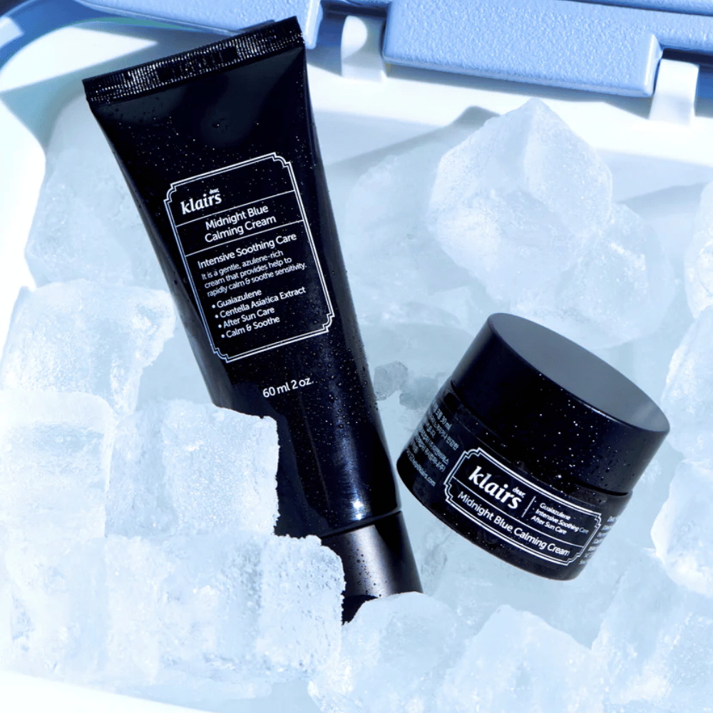 Μια σωλήνα και βάζο του Klairs Midnight Blue Calming Cream βρίσκονται πάνω σε παγάκια, με έμφαση στις καταπραϋντικές και ενυδατικές ιδιότητες, μπροστά από ένα μπλε φόντο.