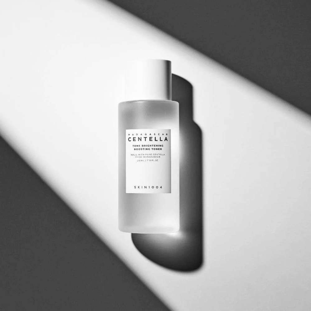 Μπουκάλι του SKIN1004 Madagascar Centella Tone Brightening Boosting Toner  που βρίσκεται σε λευκή επιφάνεια με δραματική σκιά σε ασπρόμαυρο φωτισμό.