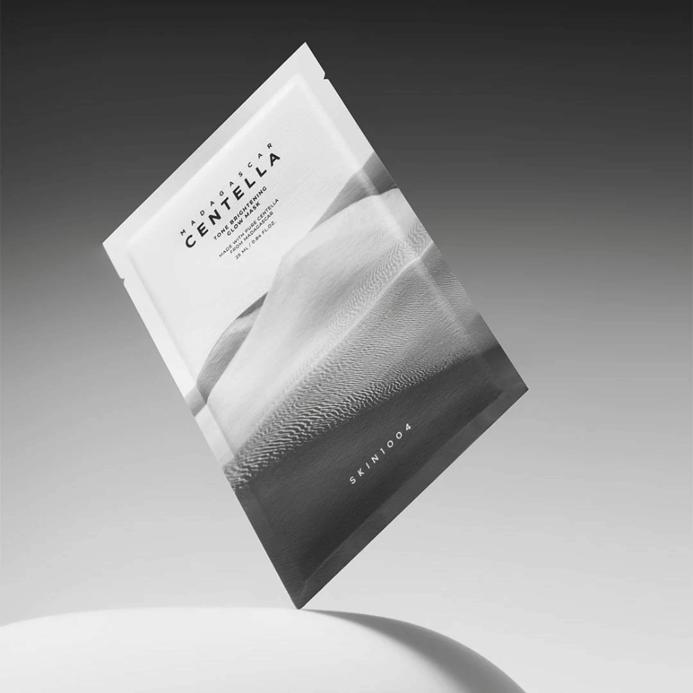 Συσκευασία sheet mask από το SKIN1004 που αιωρείται σε γκρι φόντο με μινιμαλιστικό σχεδιασμό.