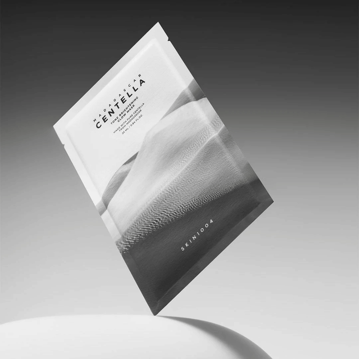 Συσκευασία sheet mask από το SKIN1004 που αιωρείται σε γκρι φόντο με μινιμαλιστικό σχεδιασμό.